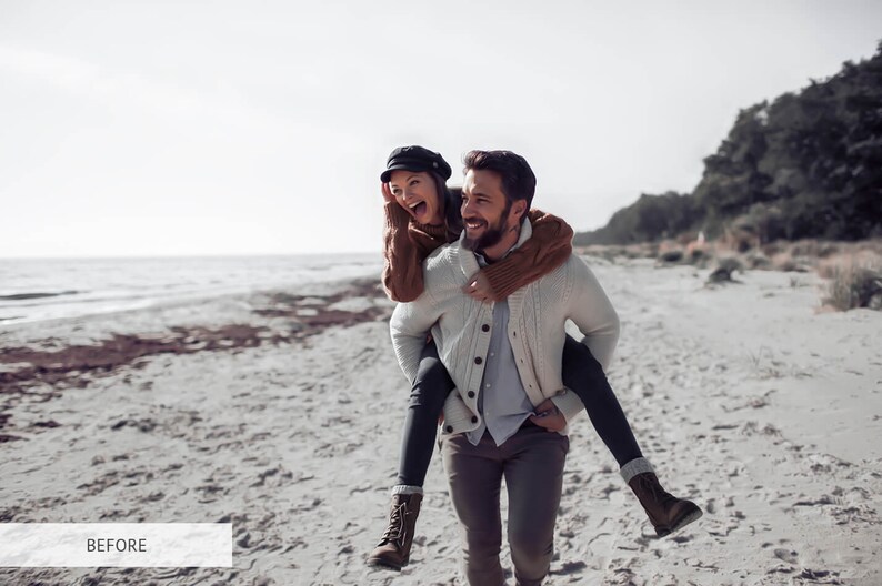 May include: A couple is walking on a sandy beach. The man is carrying the woman on his back. They are both smiling and laughing. The woman is wearing a brown sweater and a black hat. The man is wearing a white sweater and gray pants.