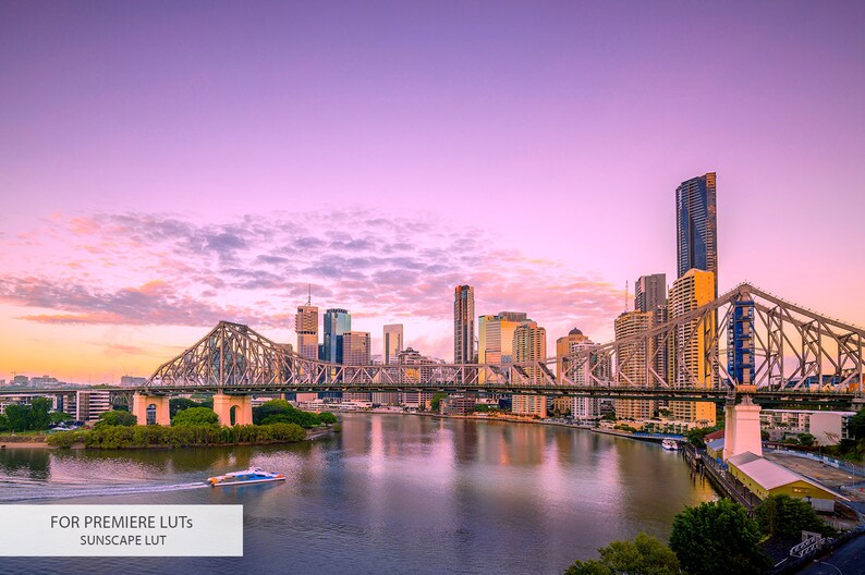 May include: A panoramic view of a city skyline at sunset with a bridge crossing a river. The sky is a vibrant pink and purple with fluffy clouds. The city buildings are tall and modern, with a few skyscrapers visible. The bridge is made of steel and has a distinctive arch design. The river is calm and reflective, reflecting the city lights.