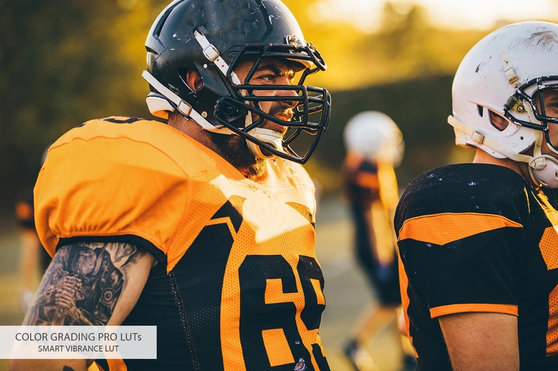 May include: Two football players wearing orange and black uniforms with helmets. The player in the foreground is looking to the right and has a tattoo on his arm.