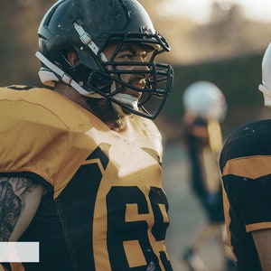 May include: Two football players wearing helmets and jerseys stand on a field. The player on the left is wearing a yellow jersey with a black number 68. The player on the right is wearing a black jersey with a yellow stripe.