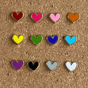 May include: Twelve gold heart-shaped pins with different colored enamel. The colors are red, pink, orange, yellow, green, blue, light blue, purple, black, white, and gray.