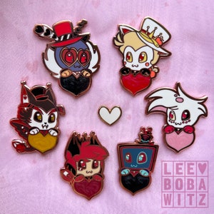 May include: Set of seven enamel pins featuring characters from the animated series 'Hazbin Hotel'. The pins are gold-toned and feature the characters holding hearts. The characters include: Angel Dust, Alastor, Valentino, Charlie, Vaggie, Sir Pentious, and the  'LEE BOBA WITZ' logo.