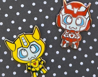 May include: Two enamel pins featuring cartoon robot characters. The first pin is yellow and features a robot with large blue eyes. The second pin is red and features a robot with large white eyes.