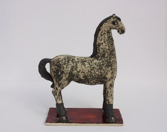 May include: A ceramic horse figurine with a white and black speckled body, black legs, and a black tail. The horse is standing on a red base.