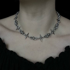 Op de afbeelding: Een zilveren ketting met scherpe, puntige spikes. De ketting is gemaakt van metaal en heeft een punkrock-esthetiek.