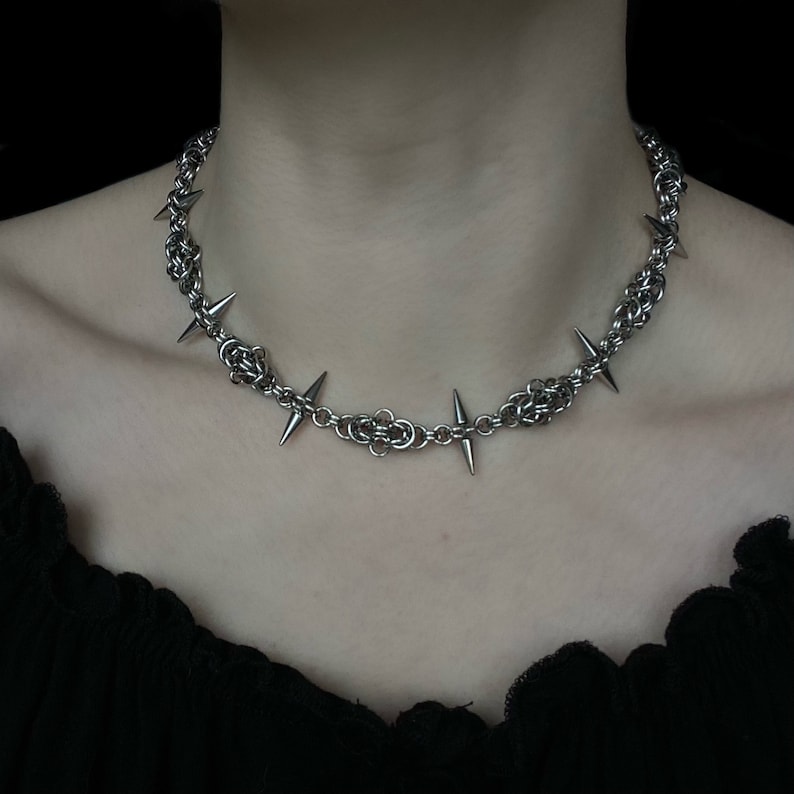 Op de afbeelding: Een zilveren ketting met scherpe, puntige spikes. De ketting is gemaakt van metaal en heeft een punkrock-esthetiek.