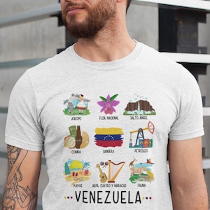 May include: A light gray t-shirt featuring colorful illustrations of Venezuelan culture, including a flag, landmarks, and traditional items. The word "VENEZUELA" is printed in a dotted font at the bottom of the shirt.