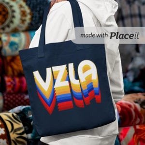 May include: A navy blue tote bag with a colorful retro design that says "VZLA" in white letters. The design is made up of yellow, orange, red, blue, and white stripes.
