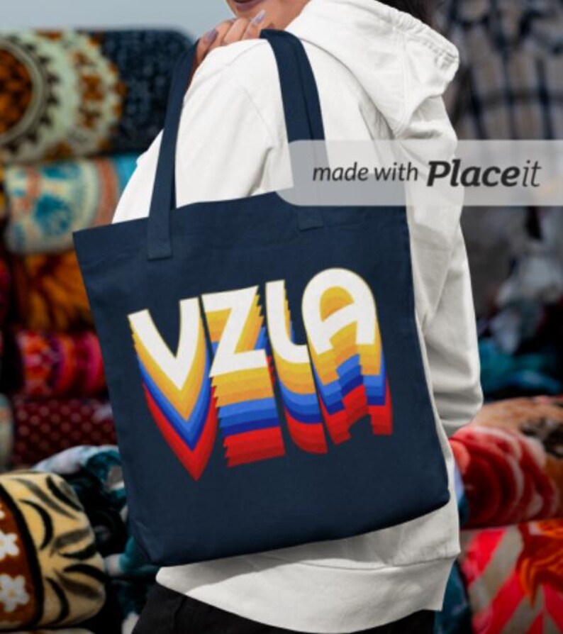 May include: A navy blue tote bag with a colorful retro design that says "VZLA" in white letters. The design is made up of yellow, orange, red, blue, and white stripes.