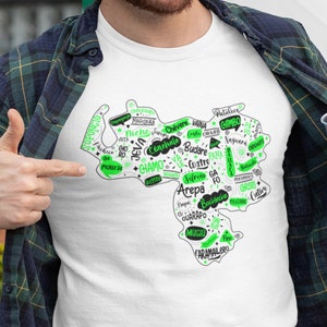 May include: White t-shirt with a green outline of Venezuela and words in Spanish, including "Arepa", "Chévere", "Jevá", "Niche", "Patuleco", "Sifrite", "Soponcio", and "Vainá".