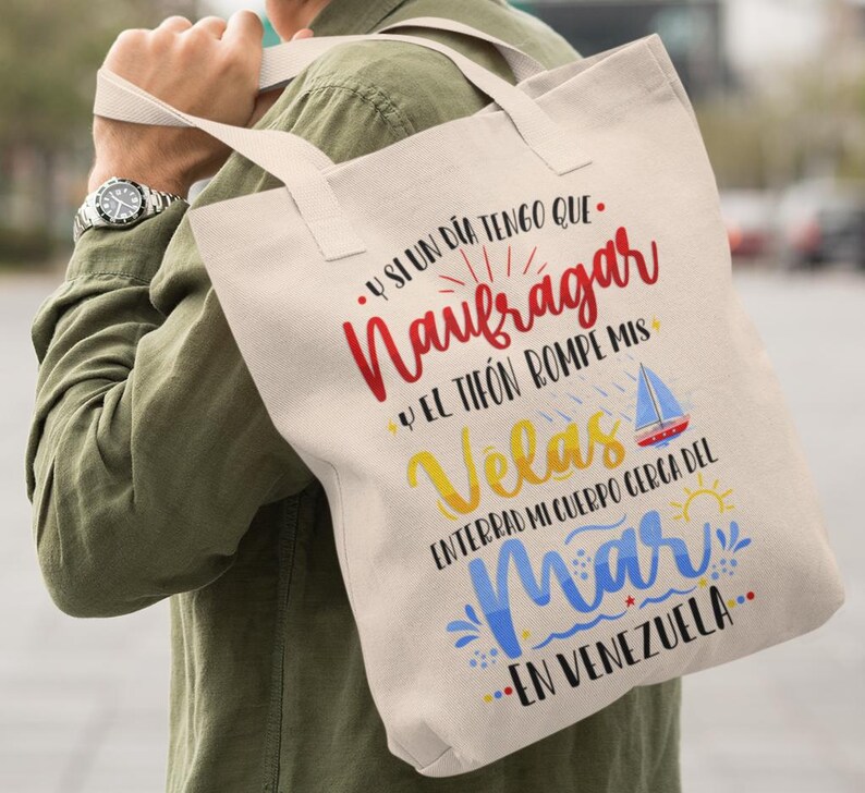 May include: A white canvas tote bag with a colourful graphic design. The text on the bag reads "Y SI UN DIA TENGO QUE. Naufragar Y EL TIF&Oacute;N ROMPE MIS Velas ENTERRAD MI CUERPO CERCA DEL Mar EN VENEZUELA."