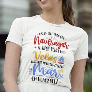 May include: White t-shirt with a colourful graphic design that says "Y si un dia tengo que Naufragar y el tif&oacute;n rompe mis Velas Enterrad mi cuerpo cerca del Mar en Venezuela."