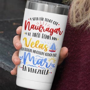 May include: White stainless steel tumbler with a colourful graphic design featuring a sailboat and the text "Y SI UN DIA TENGO QUE. Naufragar Y EL TIFON ROMPE MIS Velas ENTERRAD MI CUERPO CERCA DEL Mar EN VENEZUELA."