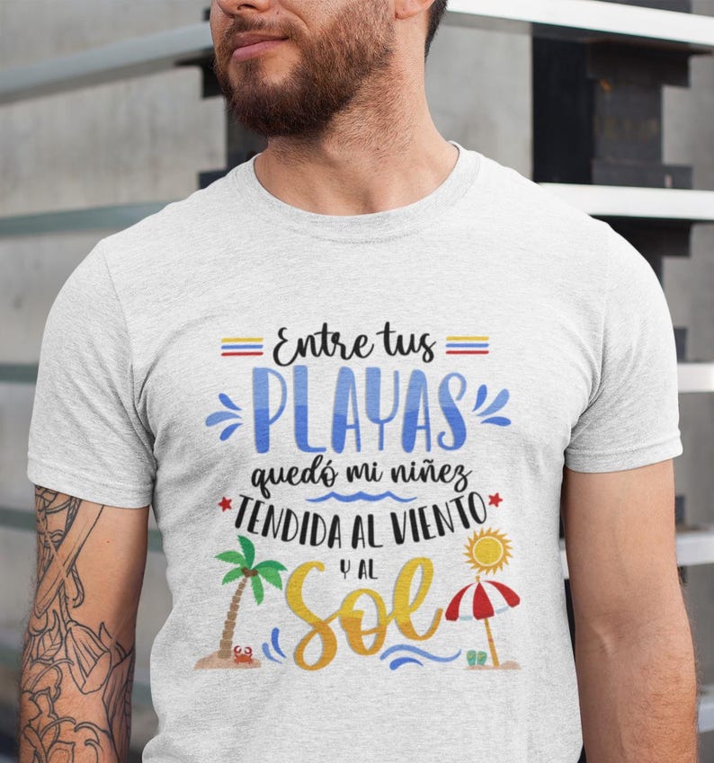 May include: White t-shirt with a graphic design featuring the text "Entre tus playas qued&oacute; mi ni&ntilde;ez tendida al viento y al sol". The graphic also includes a palm tree, a beach umbrella, and a crab.