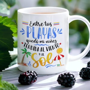 May include: White ceramic mug with a colourful design featuring the text "Entre tus PLAYAS qued&oacute; mi ni&ntilde;ez TENDIDA AL VIENTO y al SOL". The design includes a palm tree, a beach umbrella, and a sun.