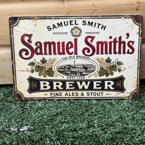 Peut inclure: Une plaque métallique rectangulaire portant les inscriptions Samuel Smith's, Tadcaster, Yorkshire, The Old Brewery, Estd 1758, Brewer et Fine Ales & Stout. Le design inclut une illustration centrale de brasserie, des houblons et une rose blanche.