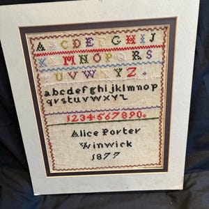 May include: Framed antique sampler with the alphabet, numbers, and the name "Alice Porter, Winwick, 1877." The sampler is stitched in various colors and framed in a brown and cream-colored frame.