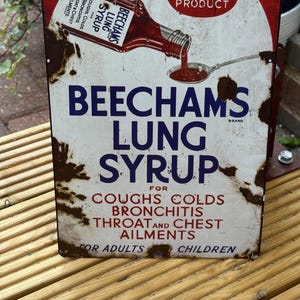 Op de afbeelding: Een rechthoekig metalen bord met een vintage reclame voor Beecham's Lung Syrup. De afbeelding toont een fles die rode siroop in een lepel giet. De tekst bevat A BEECHAM PRODUCT, BEECHAMS LUNG SYRUP en FOR COUGHS COLDS BRONCHITIS THROAT AND CHEST AILMENTS FOR ADULTS AND CHILDREN. Het bord heeft zichtbare roestvlekken.