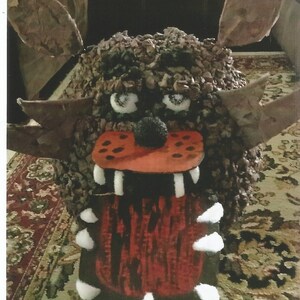 May include: A brown and red monster made of textured material with white teeth and eyes. The monster has a large, open mouth with a red tongue.