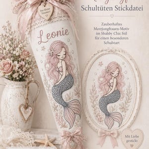 May include: A cone-shaped fabric school bag featuring an embroidered mermaid, the name Leonie, and lace trim. The design includes a matching oval embroidery hoop with a mermaid motif, pink ribbons, and text in German regarding embroidery files.