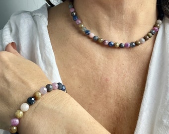 Könnte beinhalten: Ein mehrfarbiges Edelstein-Halsketten- und Armband-Set. Die Halskette und das Armband bestehen aus kleinen, runden Perlen in Blautönen, Rosa und Braun.