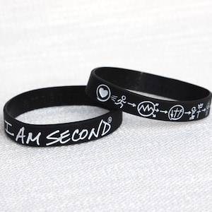 May include: Two black silicone wristbands. One says "I AM SECOND" in white lettering. The other has a heart, a running figure, and other symbols in white.
