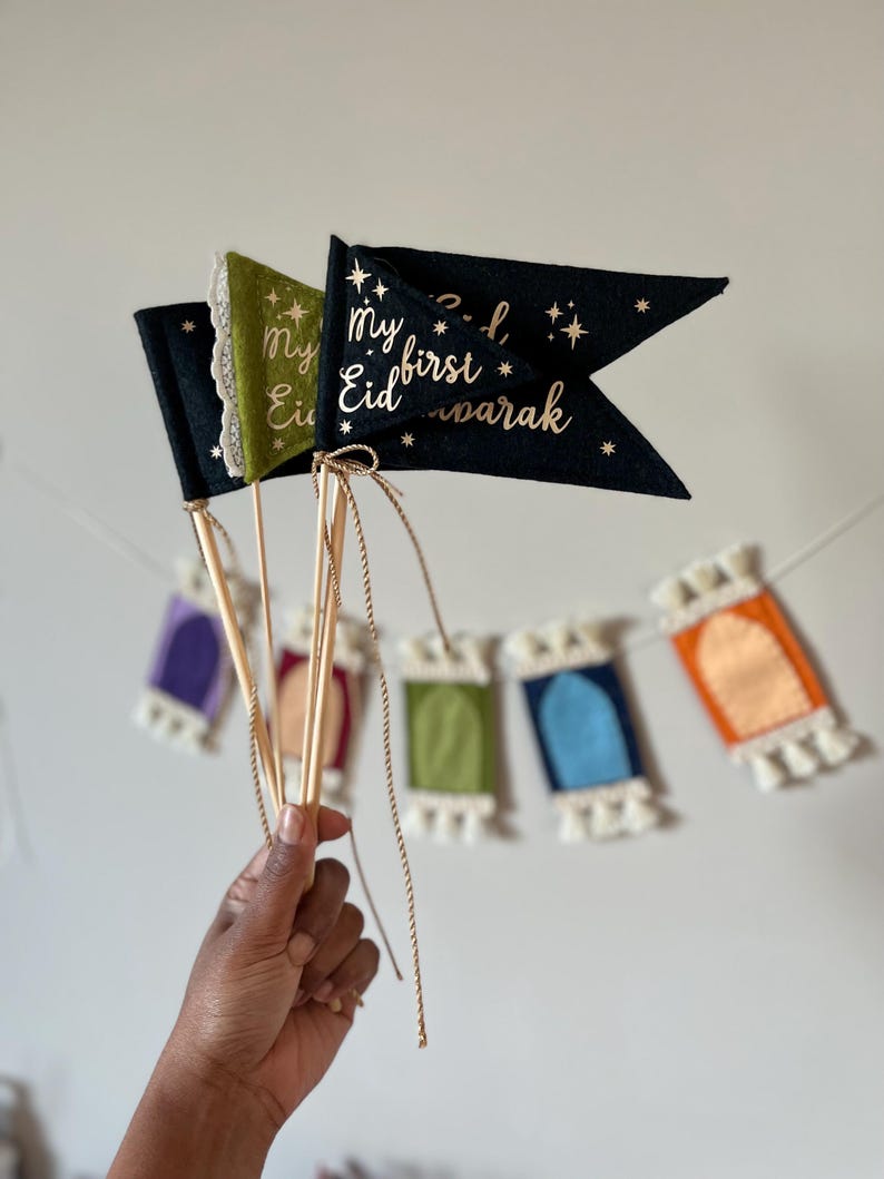 Pu&ograve; includere: Un set di tre bandiere di feltro con lettere dorate. Le bandiere sono nere, verdi e dorate. La bandiera nera dice "Il mio primo Eid Mubarak" con stelle. La bandiera verde dice "Il mio Eid".