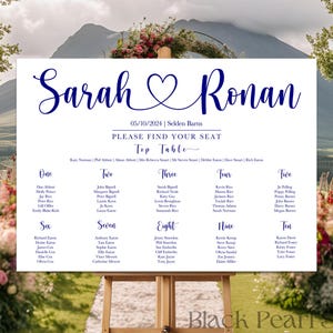 May include: A wedding seating chart on a wooden easel, with the names "Sarah & Ronan" in elegant navy blue script. The date "05/10/2024" and "Please Find Your Seat" are also displayed. The chart lists table numbers and guest names.