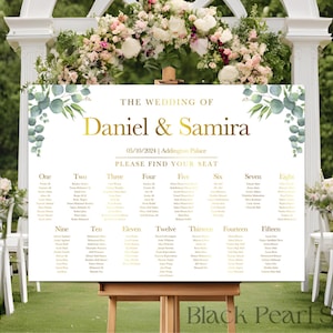 May include: A wedding seating chart with a white background and gold lettering. The chart is decorated with green eucalyptus leaves and has the names "Daniel & Samira" at the top. The chart lists tables numbered one through fifteen.