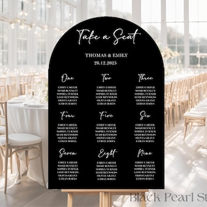 May include: Black, arched wedding seating plan with white calligraphy. The plan lists names under numbers one to nine. The top reads "Take a Seat" and "Thomas & Emily 28.12.2025".