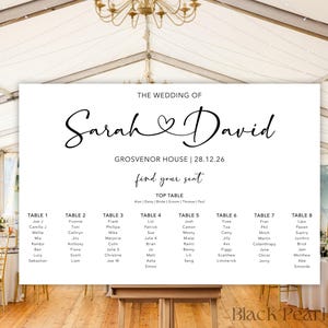 May include: A white wedding seating chart with the names "Sarah & David" in elegant script. The chart includes table assignments and the date 28.12.26. The sign is displayed in a tent setting with tables and chairs.