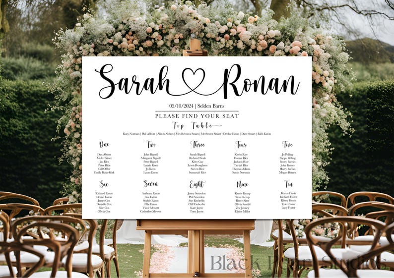 May include: A white wedding seating chart with black calligraphy text. The sign reads "Sarah & Ronan" with a heart symbol, date, and venue. Below, it says "Please Find Your Seat" and lists table numbers and guest names. The sign is displayed on a wooden easel.