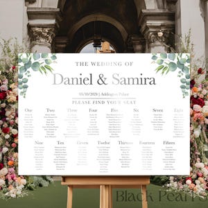 May include: A wedding seating chart with a white background and green eucalyptus leaves on the top and bottom. The chart is titled "The Wedding of Daniel & Samira" with the date "06/10/2024" and location "Addington Place". The chart lists table numbers from one to fifteen with guest names under each table number.