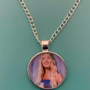 Puede incluir: Collar plateado con un colgante redondo que presenta una imagen en color de una mujer con cabello rubio largo. La cadena es de estilo eslabón clásico, y el colgante está engastado en un bisel plateado.