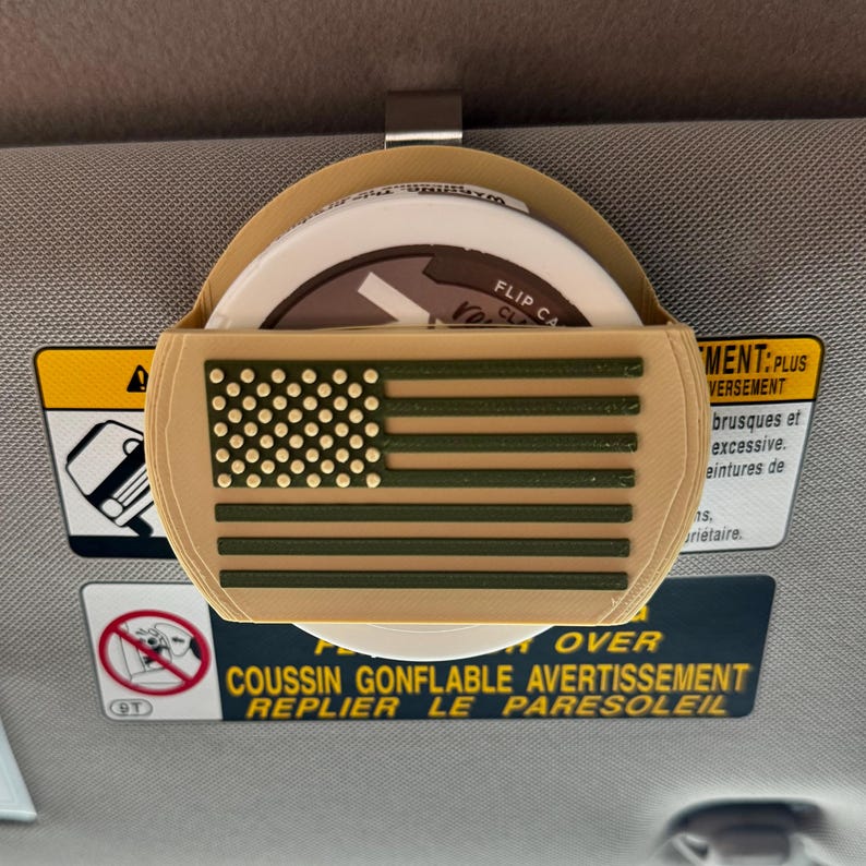 May include: A tan car visor organizer with an American flag design in olive green. The organizer holds several round items and has a metal clip for attachment. The text "FLIP CA" is visible.