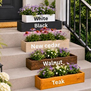 May include: A display of rectangular wooden planters in various colors: white, black, new cedar, walnut, and teak. Each planter is filled with colorful flowers, creating a vibrant outdoor scene. The text on the planters indicates their color.