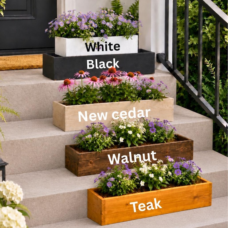 May include: A display of rectangular wooden planters in various colors: white, black, new cedar, walnut, and teak. Each planter is filled with colorful flowers, creating a vibrant outdoor scene. The text on the planters indicates their color.