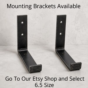 May include: Two black metal mounting brackets with a 6.5-inch size, each featuring a right-angle design with pre-drilled holes for easy installation. The text "Mounting Brackets Available" and "Go To Our Etsy Shop and Select 6.5 Size" are visible.