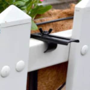 May include: Black metal plant hanger bracket with a white plastic fence post in the background. The bracket has a screw and a nut to secure it to the fence post.