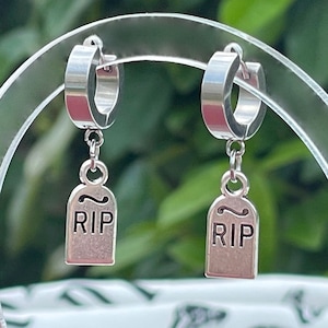 May include: A pair of silver hoop earrings with a dangling silver charm that reads "RIP".