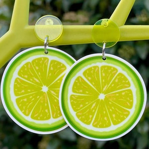 May include: A pair of lime green earrings with a lime slice design. The earrings are made of acrylic and have a silver hook.