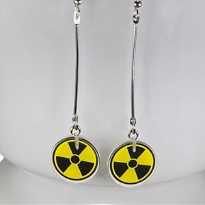 May include: A pair of silver dangle earrings with black and yellow radiation symbol charms.