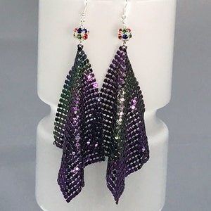 May include: A pair of long, dangling earrings with a purple and green iridescent finish. The earrings are made of a chainmail-like material and feature a small, multi-colored crystal at the top.
