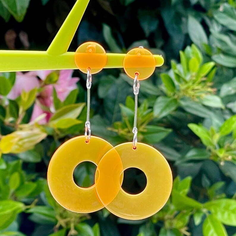May include: A pair of yellow and orange acrylic earrings with a circle design. The earrings are hanging from silver hooks.