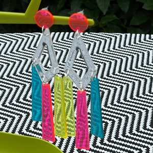 May include: A pair of silver geometric earrings with dangling neon pink, yellow, and turquoise acrylic pieces.