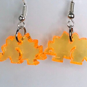 May include: A pair of orange acrylic dinosaur earrings with silver hooks.