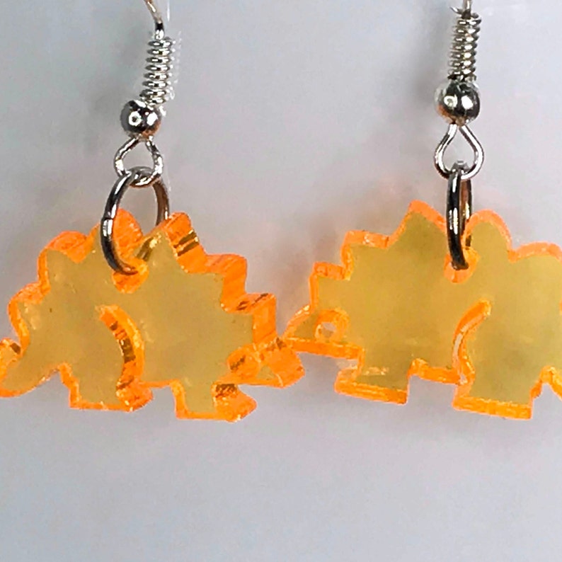 May include: A pair of orange acrylic dinosaur earrings with silver hooks.