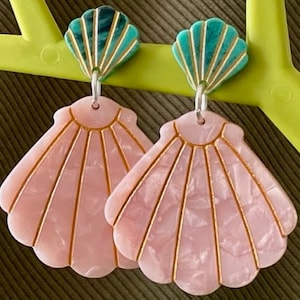 May include: A pair of drop earrings featuring a small teal marbled shell stud connected by a silver ring to a larger, fan-shaped pink marbled shell pendant. Each shell piece is detailed with thin, vertical gold-coloured lines etched into the surface.