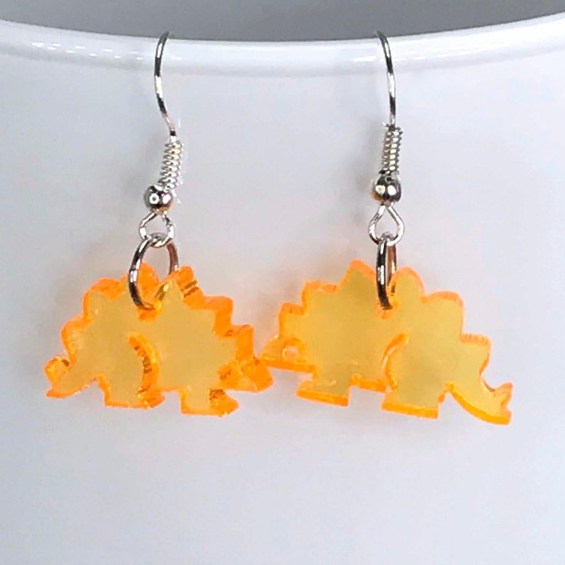 May include: A pair of orange dinosaur shaped earrings with silver hooks.