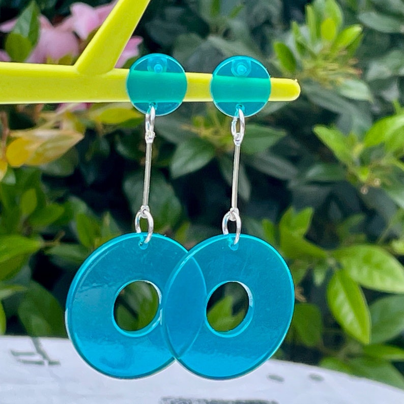May include: A pair of turquoise blue dangle earrings with a large circular pendant. The earrings have a silver chain and a smaller turquoise blue circle at the top.